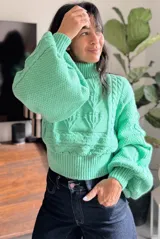 Polera de tejido de punto color verde menta, con cuello alto, diseño de trenzas y mangas abullonadas con puños ajustados.