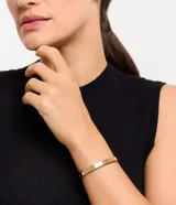 Pulsera rígida dorada de metal con forma ovalada.