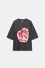Camiseta de corte oversize con efecto lavado, cuello redondo y manga corta. Presenta una estampa gráfica central que representa una figura femenina sobre un pastel decorado con cerezas.