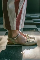 Sandalias de cuero color celeste, con punta cerrada, flecos frontales y detalle de estribo metálico dorado. Tienen tira ajustable al tobillo y suela plana con pequeño taco.