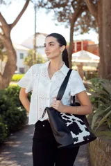 Bolso tote de cuero negro con panel central de cuero con estampado animal print de vaca en blanco y negro. Tiene doble asa de cuero y el logo de la marca grabado en el lateral.