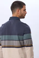 Remera polo de manga larga con diseño de franjas horizontales en tonos azul, gris y detalles en bordó. Presenta cuello camisero con cierre de botones y puños elásticos.