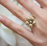 Anillo dorado con forma de flor, compuesto por siete esferas de diferentes tamaños.