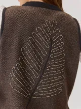 Chaleco de paño con diseño bicolor, frente en color negro y espalda en color marrón con textura de espiga. Presenta un maxi bordado de hoja en la parte posterior y detalles de tejido en los bordes.