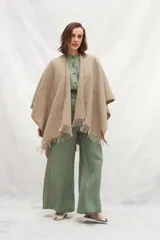 Ruana de lana 100% sin teñir en color tostado, con diseño de punto acanalado y terminación de flecos en el ruedo.