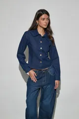 Campera corta de denim azul oscuro con cuello camisero, mangas largas y cierre frontal de botones metálicos dorados.