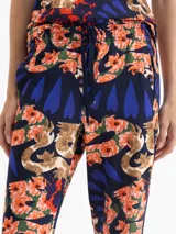 Babucha de algodón con estampado floral y de serpientes en tonos naranja, azul y verde sobre fondo azul marino. Tiene cintura elastizada con cordón ajustable y calce regular.