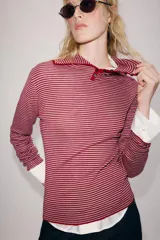 Jersey de punto confeccionado en hilatura con lana, con diseño de rayas horizontales en tonos rojo y gris. Presenta cuello solapa, escote en V y detalle de botones decorativos en el cuello y la solapa.
