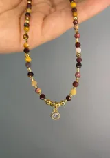 Collar con cuentas de piedra natural jaspe australiano en tonos borbón y mostaza, intercaladas con cuentas doradas, y un dije central redondo con piedra translúcida.