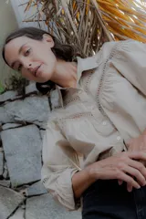 Camisa de algodón color beige con detalles de encaje y broderie en el canesú y las mangas. Presenta cuello camisero, cierre frontal con botones y mangas largas con puños.