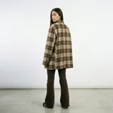 Blazer de corte oversize con estampado de cuadros en tonos negro y beige. Presenta solapas clásicas, cierre frontal con botones y bolsillos laterales con solapa.