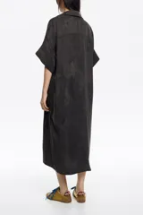 Vestido camisero largo de corte holgado y fluido, con cuello camisero, cierre frontal de botones y mangas cortas. Presenta bolsillos frontales tipo parche en el pecho y a la altura de la cadera.