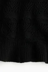 Musculosa corta negra de punto crochet con escote redondo pronunciado con ribete festoneado y bajo acanalado de volado. Sin mangas.