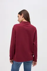 Remera tipo polo de manga larga en color beige, confeccionada en algodón pesado con textura suave. Presenta cuello clásico, cierre frontal con botones y un pequeño bordado en el pecho. Posee puños en las mangas y un corte relajado.