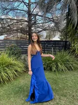 Vestido largo de satén color marrón con acabado metalizado, escote en V, tirantes finos cruzados en la espalda y diseño con corte bajo el busto y volados en la falda.