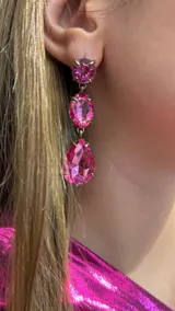 Caravanas colgantes compuestas por tres cristales facetados en color fucsia, con engarce metálico en tono bronce. El diseño presenta un cristal circular superior, uno ovalado central y uno en forma de gota en la parte inferior.