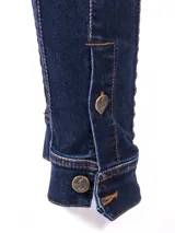 Pantalón de jean chupín azul oscuro con costuras marcadas al frente y detalle de botones dorados en los tobillos.