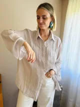 Camisa de manga larga en color visón claro, con diseño de tablitas verticales y detalles de puntilla. Presenta cierre frontal con botones de nácar y cuello camisero clásico.