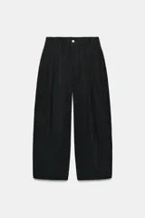 Pantalón fluido de tiro medio, color negro, con cintura elástica, bolsillos laterales ocultos, pinzas en el delantero y cierre frontal con cremallera y botón.