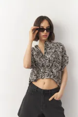 Blusa corta de manga corta con estampado en blanco y negro, cuello mao y cierre frontal con botones. Cuenta con detalle de elástico fruncido en la cintura que genera un efecto peplum.