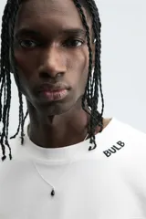 Camiseta de algodón blanca con corte relajado y cuello redondo. Presenta un pequeño bordado en negro con la palabra "BULB" en la parte superior del pecho.