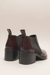 Botín chelsea de cuero vacuno color bordó con acabado charol, punta fina y elástico lateral negro. Posee un taco ancho y bajo de goma.