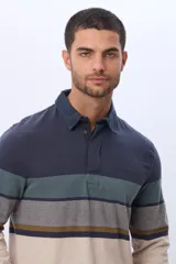 Remera polo de manga larga confeccionada en algodón con diseño de franjas horizontales en tonos azul marino, verde militar, gris, mostaza y beige. Cuenta con cuello camisero y cierre frontal parcial con botones.