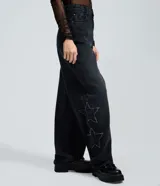 Pantalón de jean color negro con corte baggy y cintura media. Presenta estrellas bordadas con acabado desflecado en las piernas y bolsillos funcionales.