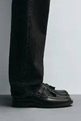 Mocasín de vestir negro con detalle de borlas en la parte superior, forro y plantilla interior a tono, horma redonda y suela con ligero tacón.