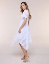 Vestido midi blanco de estilo romántico confeccionado en poliéster con elastano, con detalles de encaje floral. Cuenta con escote cruzado en V, mangas cortas acampanadas, cintura elastizada y falda evasé con terminación asimétrica en picos.