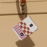 Billetera porta tarjetas elástica con diseño a cuadros color naranja y blanco en la parte superior y a cuadros color lila y blanco en la parte inferior. Incluye llavero de metal dorado.