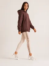 Hoodie Trena de frisa color marrón chocolate, con moldería oversize, hombros caídos, capucha con cordones ajustables y bolsillo tipo canguro. Presenta puños y ruedo de rib elástico, y detalles de bordado en la manga.