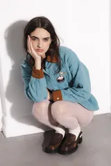 Campera celeste con cuello y puños de pana color marrón. Tiene cierre con botones a presión dorados, bolsillos frontales y parches bordados en el pecho.