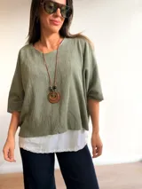 Conjunto de dos piezas compuesto por una remera básica blanca de algodón y un buzo liviano de textura plisada en color azul grisáceo. El buzo presenta un diseño de manga murciélago, corte holgado y detalles de hilo plateado en los bordes. Incluye un collar largo con dije circular de madera y metal.