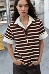 Top de estilo polo con mangas cortas, confeccionado en tejido de punto con diseño de rayas horizontales en tonos marrón y crema. Presenta cuello clásico y puños en contraste de color blanco en popelín, con cierre frontal de un botón y aberturas laterales en el bajo.