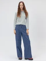 Pantalón de tiro medio y pierna ancha confeccionado en denim de algodón grueso. Presenta un diseño a rayas verticales en tonos azul y celeste, con costuras en contraste color rojo, bolsillos laterales tipo cargo y remaches metálicos.
