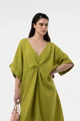 Vestido midi marrón de lino, con escote en V, mangas cortas amplias y detalle fruncido en el centro del frente. Presenta diseño asimétrico con dobladillo más largo en la parte trasera y corte relajado.