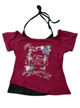Remera bordó de manga corta con diseño de hombros descubiertos (off-shoulder) y un detalle superpuesto tipo bikini negro en el cuello. Cuenta con un estampado gráfico frontal de estilo vintage con flores y texto.