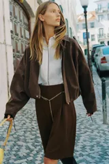 Bermuda de tiro alto color marrón oscuro, con pliegues frontales y bolsillos laterales ocultos. Incluye un cinturón metálico fino de cadena dorada que cruza la cintura.