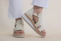 Sandalias de cuero color marfil, con plataforma de 4 cm en tonos beige y blanco, tiras anchas en el empeine con aberturas laterales y tira ajustable en el tobillo con hebilla.