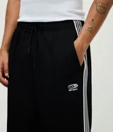 Pantalón deportivo negro con rayas laterales blancas, cintura elástica, bolsillos y estampa localizada en la parte superior.