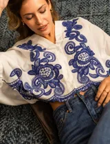 Blusa blanca de algodón con bordados azules, escote en V, cierre frontal con botones y mangas 3/4 dolman.