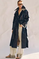 Trench oversize de efecto piel color azul marino, con cuello solapa, manga larga, bolsillos delanteros y cinturón ajustable del mismo tejido. Cierre frontal cruzado con botones y forro interior.