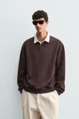 Sudadera tipo polo de corte regular, color gris claro, con cuello solapa en color blanco y cierre frontal de botonadura oculta. Presenta mangas largas con puños y ruedo en rib.