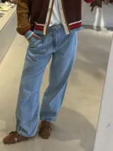 Jean de corte holgado y tiro medio, con diseño de pinzas en la cintura y detalle de botones en el ruedo que permite ajustar la botamanga.