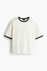 Remera de algodón en color blanco con cuello y bordes de mangas en contraste color negro. Presenta un diseño de corte holgado con hombros caídos y bajo recto.