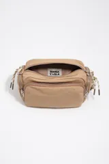 Bolso tipo morral Bimba y Lola, de color tostado, confeccionado en nylon suave con detalles en cuero y tirantes de cordón. Cuenta con múltiples compartimentos con cierre y el logo metálico de la marca en el frente.