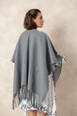 Ruana abierta de color beige, confeccionada en tejido de punto con terminación de flecos en el ruedo.