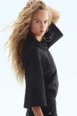 Saco de punto suave color gris oscuro, con cuello camisero y botones frontales. Presenta un diseño de hombros caídos y mangas holgadas que terminan por debajo del codo.