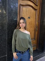 Buzo de cuello bote con diseño de hombro descubierto, confeccionado en tela angorina elastizada. Presenta un corte amplio en la parte superior y ajustado en la cintura, con mangas largas.